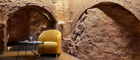 A room with a brick wall, a yellow armchair, and a small table with a book and a glass.