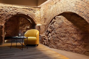 A room with a brick wall, a yellow armchair, and a small table with a book and a glass. - Hotel HCC Taber (Barcelona)