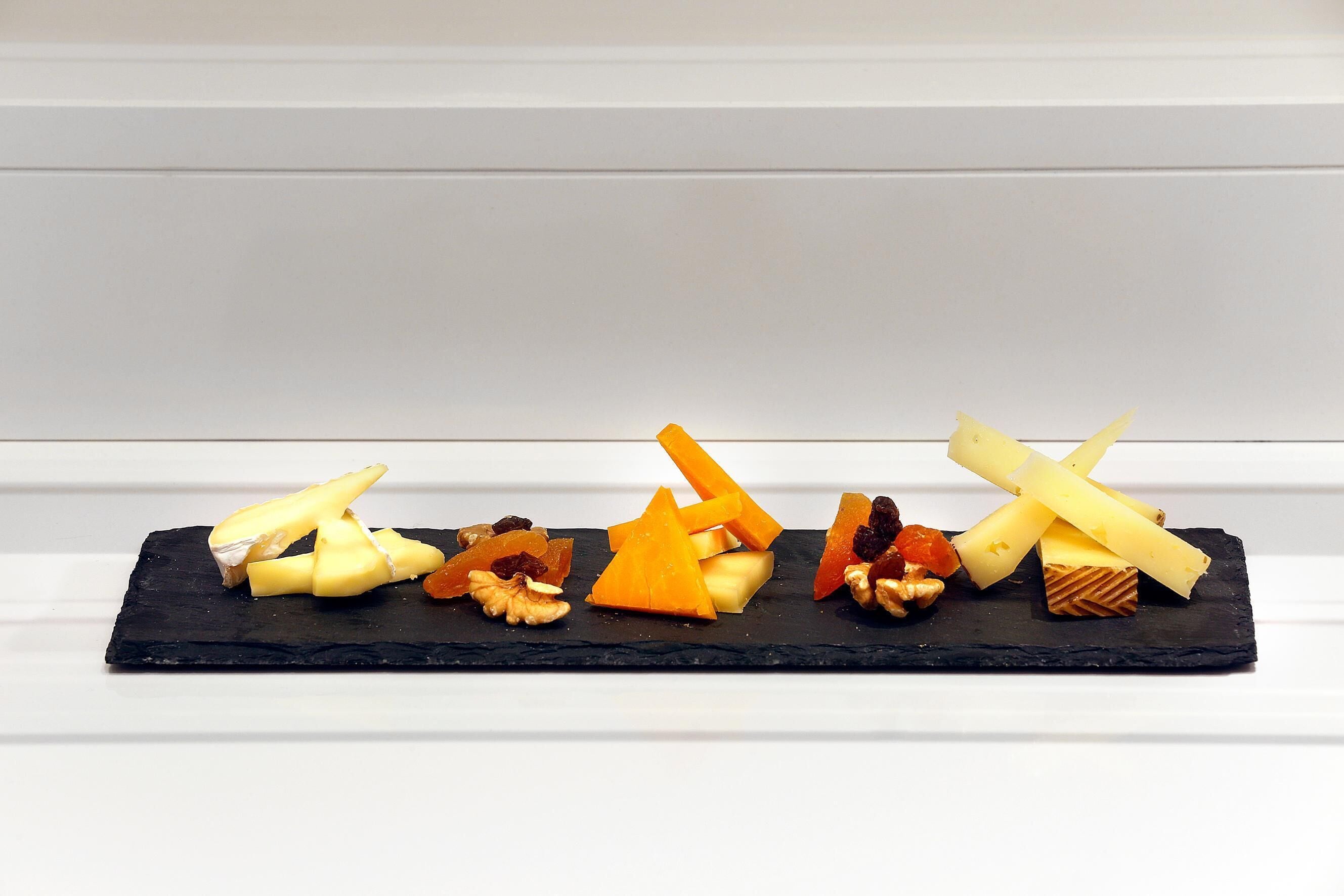 A black slate board with various cheeses and nuts.
