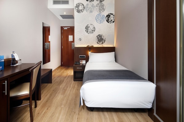 A hotel room with a bed, a desk, and a chair. There is a wall with circular patterns and a nightstand with a lamp.