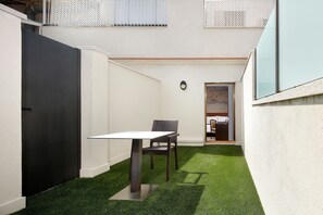 Eine kleine Terrasse im Freien mit Tisch und Stuhl, umgeben von weißen Wänden und einem schwarzen Tor.