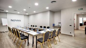Un salón de conferencias con una larga mesa, sillas, una pizarra y un cartel de HccHotels Barcelona.