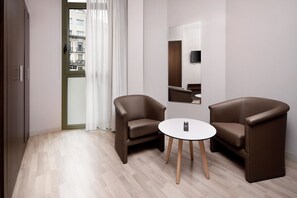 A modern room with two brown leather armchairs, a small round table, a mirror on the wall, and a view of buildings through a door. - Hotel HCC Taber (Barcelona)