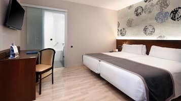 Habitación de hotel con cama, escritorio, silla y televisor montado en la pared.