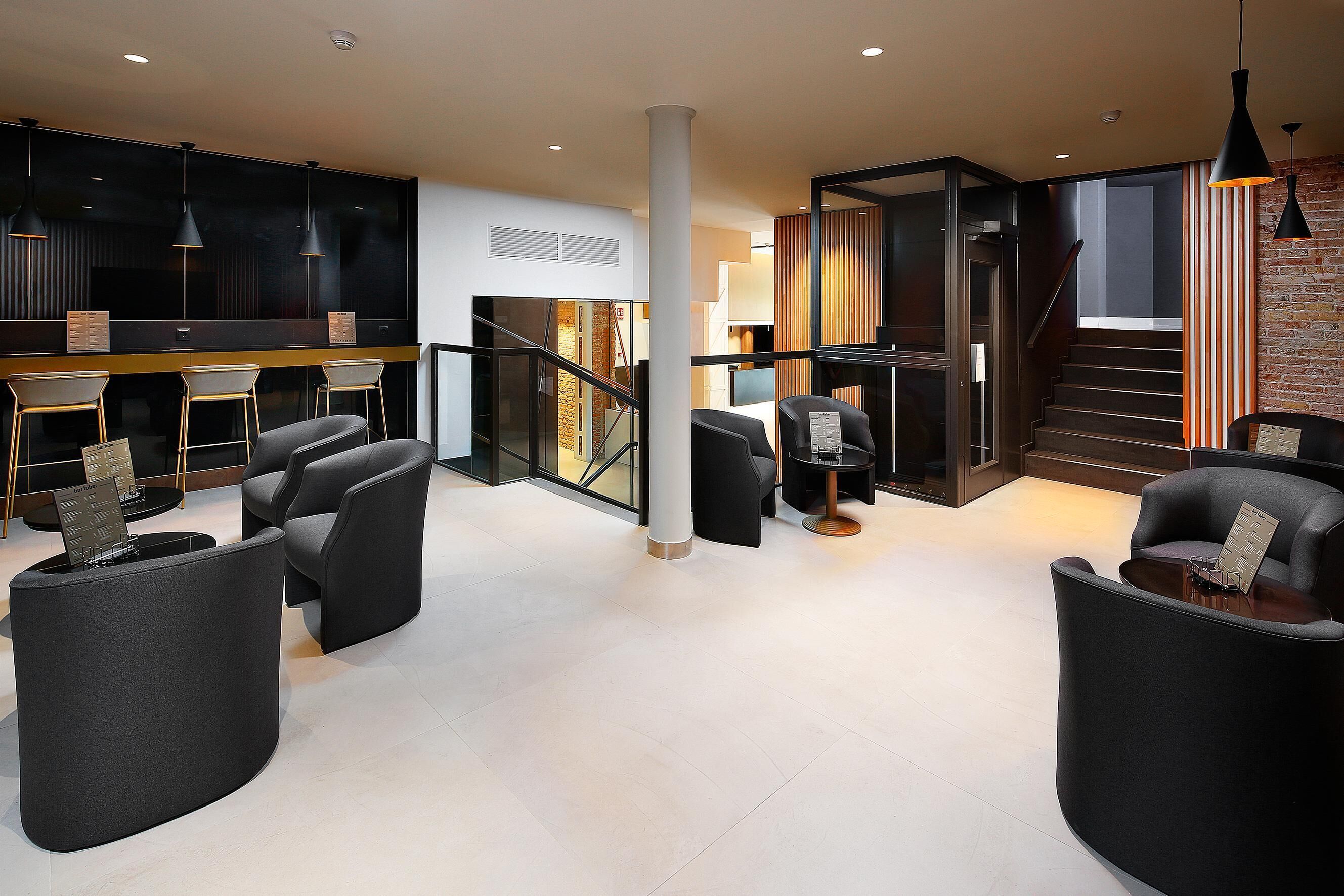 Un interior moderno con una escalera, muebles negros y una zona de bar.