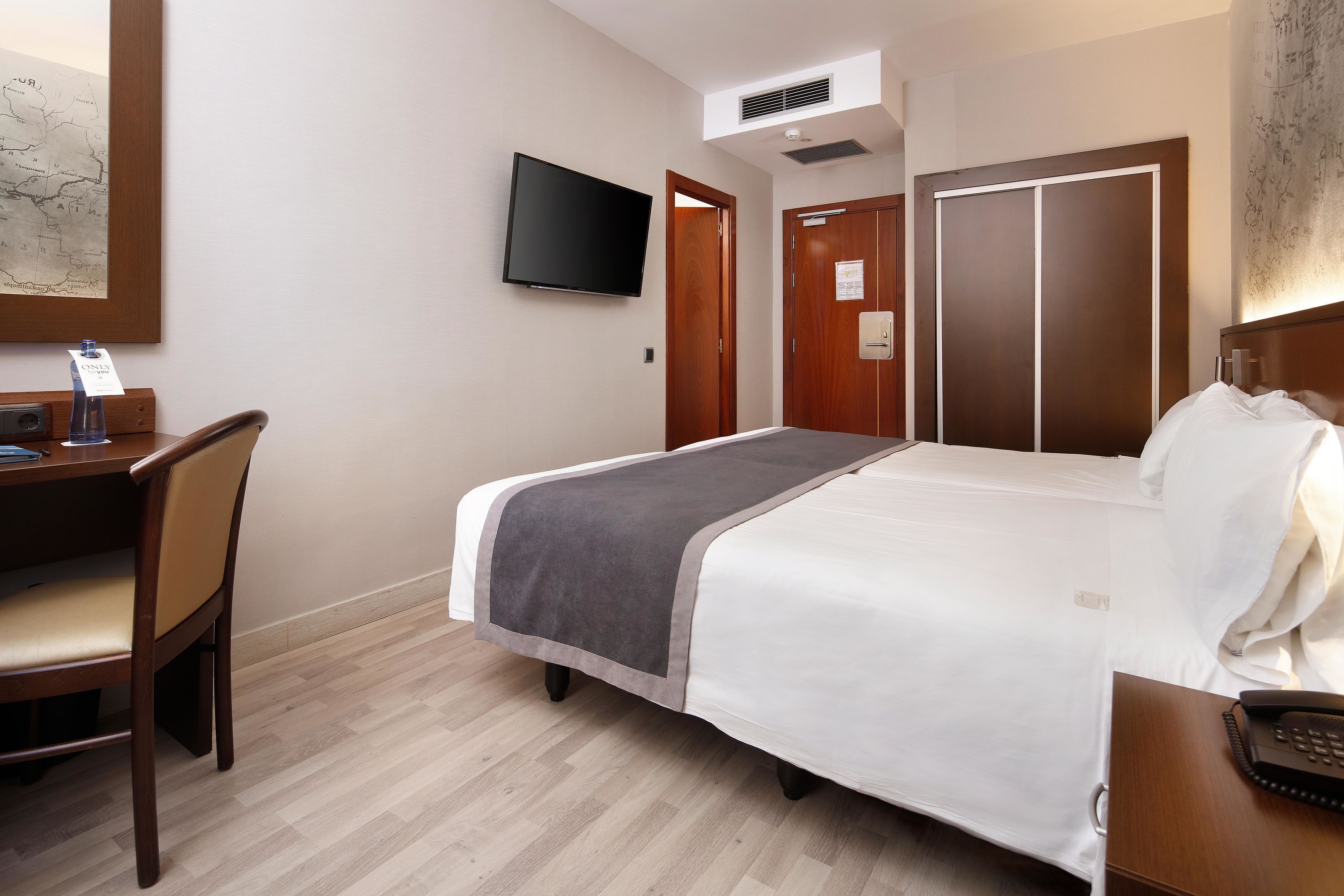 A hotel room with a bed, a desk with a chair, a television, and a wardrobe.