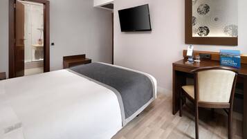 Habitación de hotel con cama, escritorio, silla, televisión y baño visible a través de una puerta abierta.