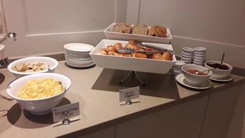 Un bufé con diversas opciones de comida, incluyendo bollos daneses, cereal sin gluten y tazones de sopa.