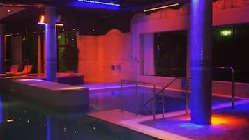 An indoor swimming pool with a tiled floor, a glass wall, and a metal railing.