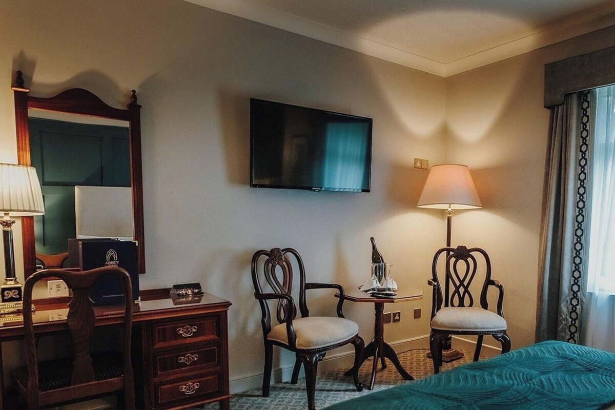 A hotel room with a bed, two chairs, a desk, a television, and a window with curtains.