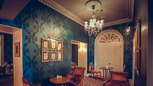 A room with a patterned blue wall, a chandelier, framed pictures, and a white door. - Abbey Hotel Roscommon (Roscommon)