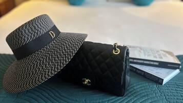 A bed with a teal comforter, two pillows, a black quilted handbag, a black hat, and a pair of glasses on the bed.
