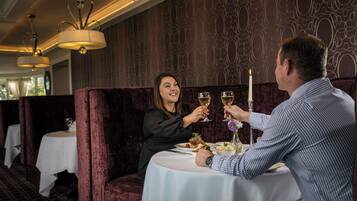 A couple seated at a table with a candle, surrounded by dark patterned wallpaper and elegant lighting fixtures.