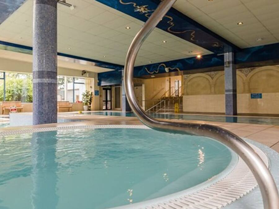 An indoor swimming pool with a curved glass barrier, a tiled column, and a staircase in the background.