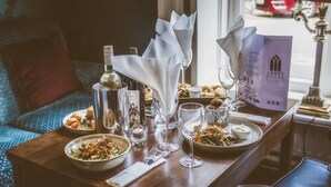 A dining table set with various dishes, glasses, and bottles, with a menu and a lamp in the background. - Abbey Hotel Roscommon (Roscommon)