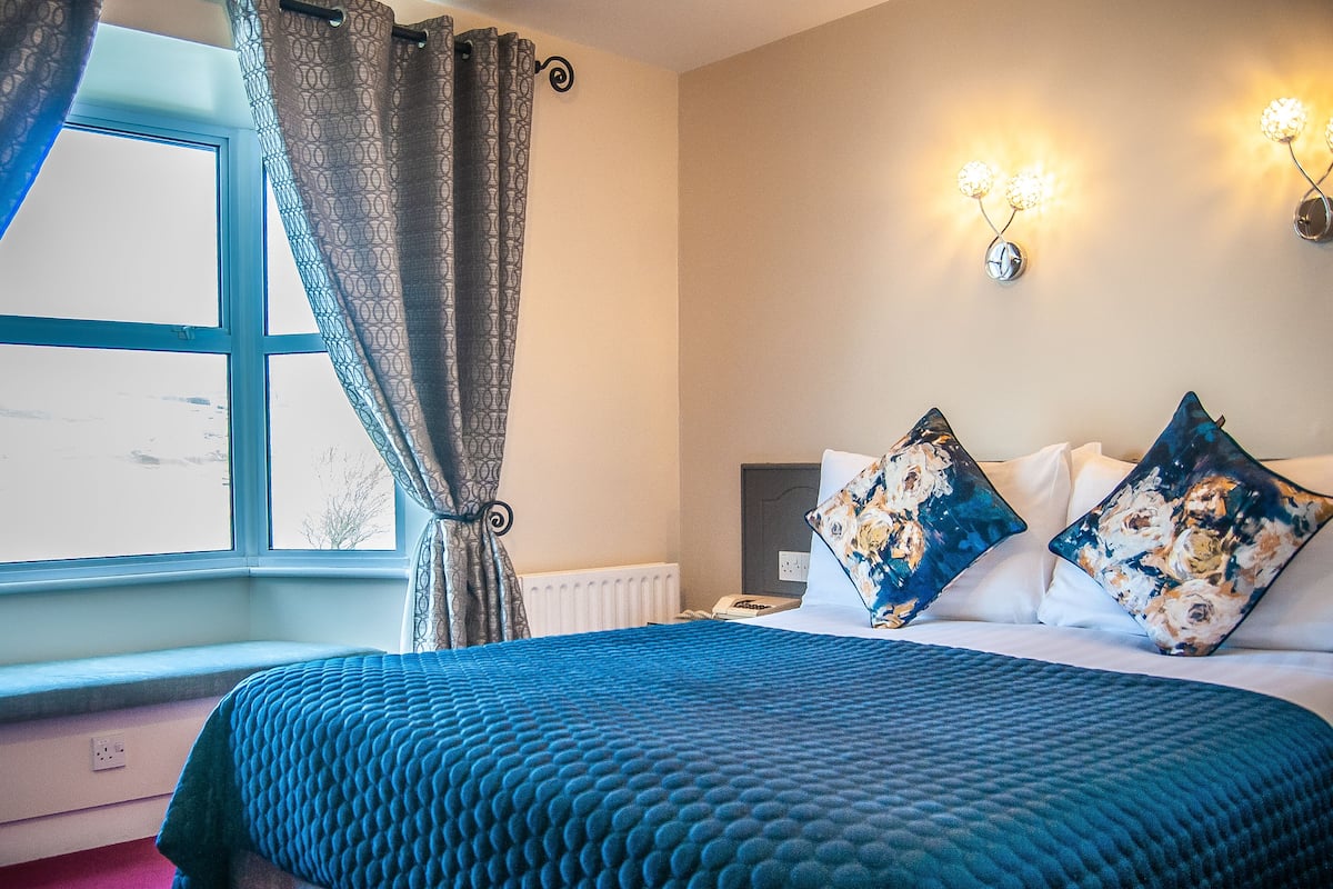Une chambre avec un grand lit, une fenêtre avec des rideaux, un radiateur et des lampes fixées au mur.