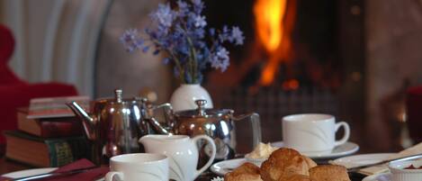 A table set with tea service, including a teapot, cups, and scones, with a fireplace in the background.
