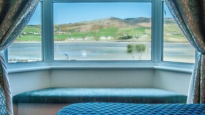 Quarto com uma grande janela que oferece vista para uma paisagem costeira, incluindo colinas e um corpo de água.