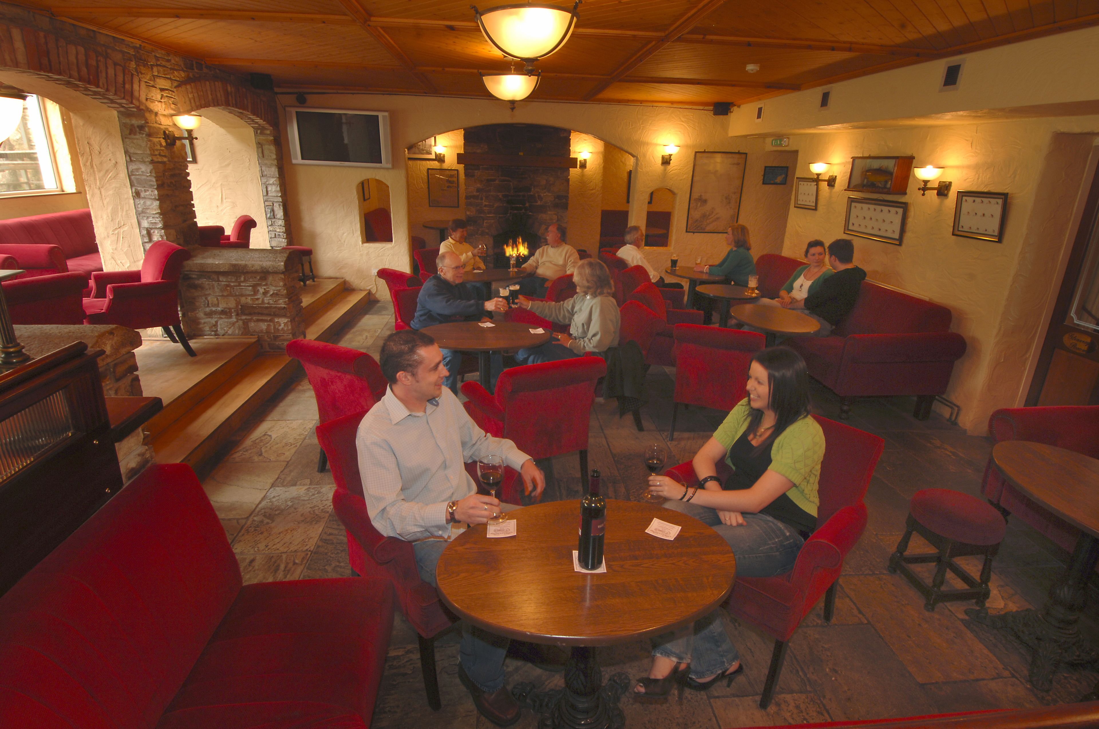 Un restaurante acogedor con sillas tapizadas en rojo, una chimenea de piedra y techo de madera.