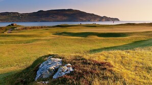 Um campo de golfe com um corpo d'água e colinas ao fundo.