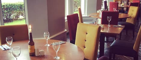 Un comedor con mesas redondas, sillas, copas de vino y botellas.