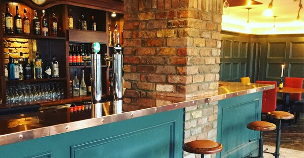 A bar area with a brick wall, shelves with bottles, and stools.