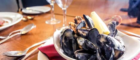 A bowl of mussels on a table with a red napkin, wine glasses, and cutlery.