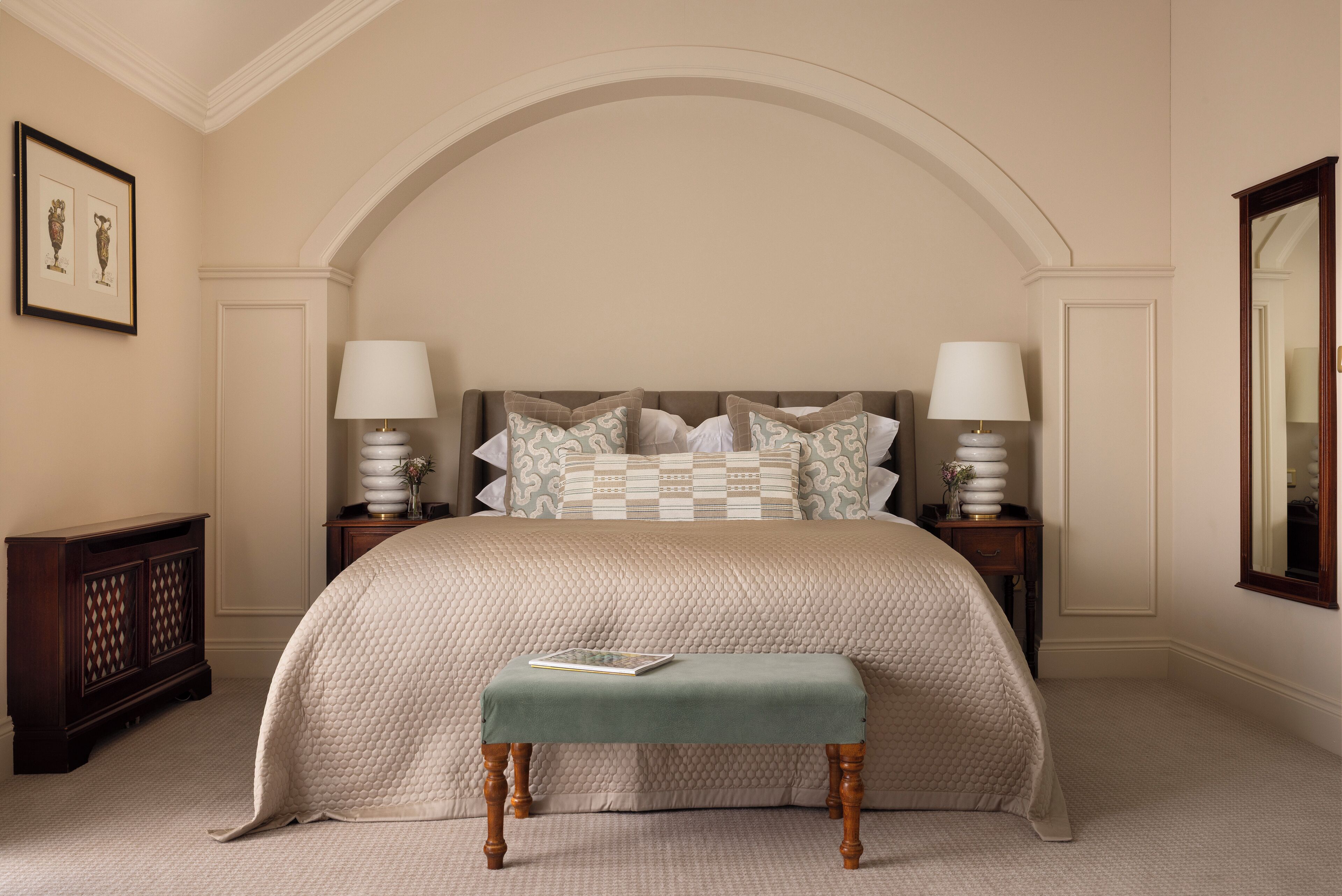 A bedroom with a large bed, two bedside tables with lamps, a bench, and a framed picture on the wall.