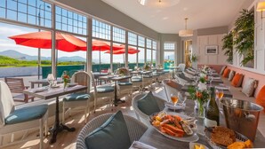 A restaurant with outdoor seating, large windows, and a view of the mountains.