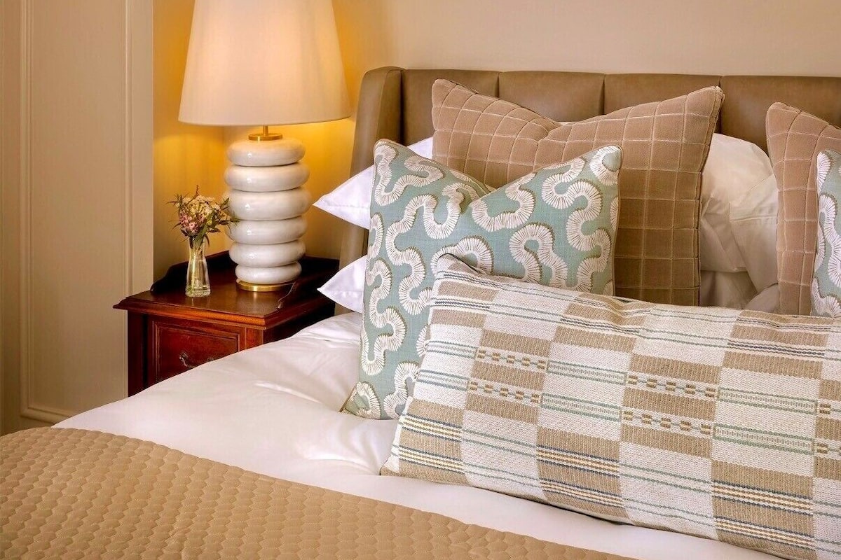 A neatly made bed with patterned pillows, a bedside lamp, and a small vase of flowers.