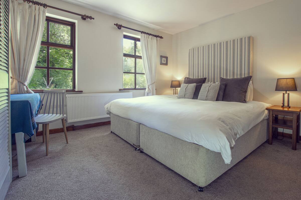 A bedroom with a large bed, two bedside tables with lamps, a chair, and a window with curtains.