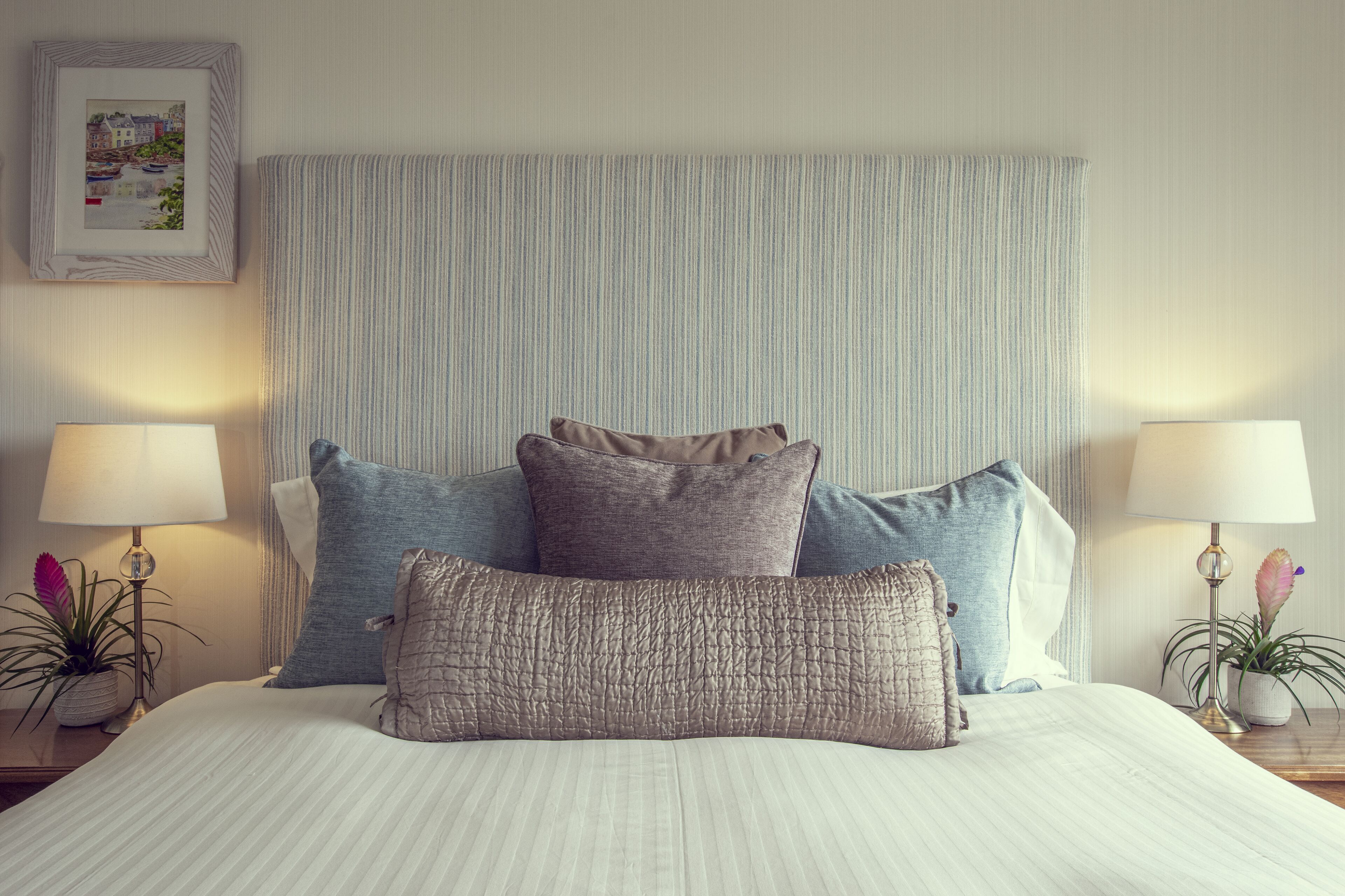 A neatly made bed with striped bedding, two bedside lamps, and a framed picture on the wall.