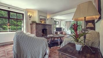 A cozy living room with a fireplace, comfortable seating, and a large window offering a view of greenery.