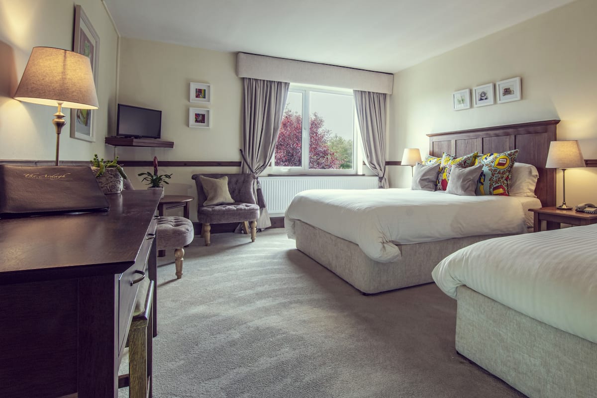 A hotel room with two beds, a desk, a chair, a TV, and a window with curtains.