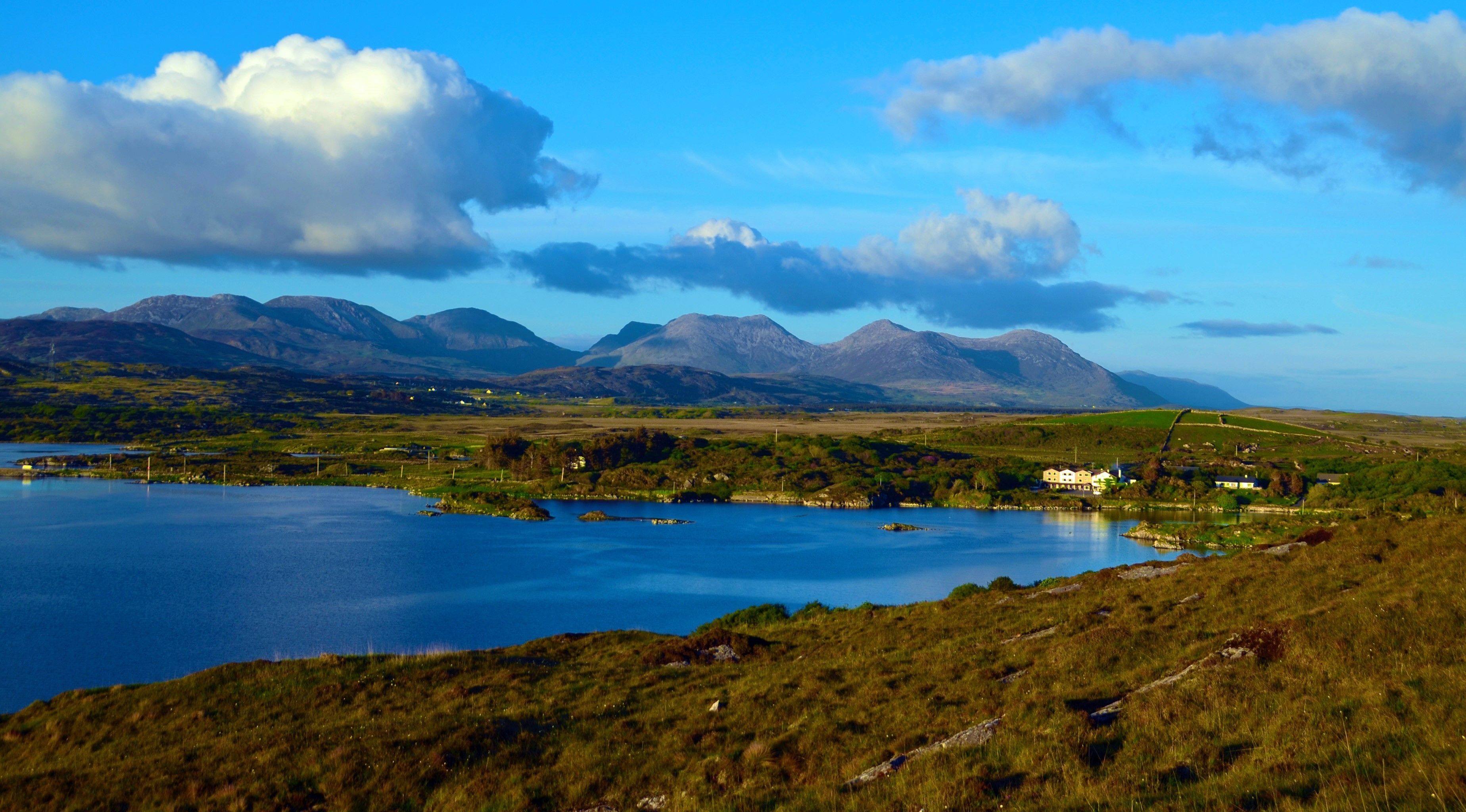 A scenic landscape with a lake, mountains, and a small cluster of buildings.