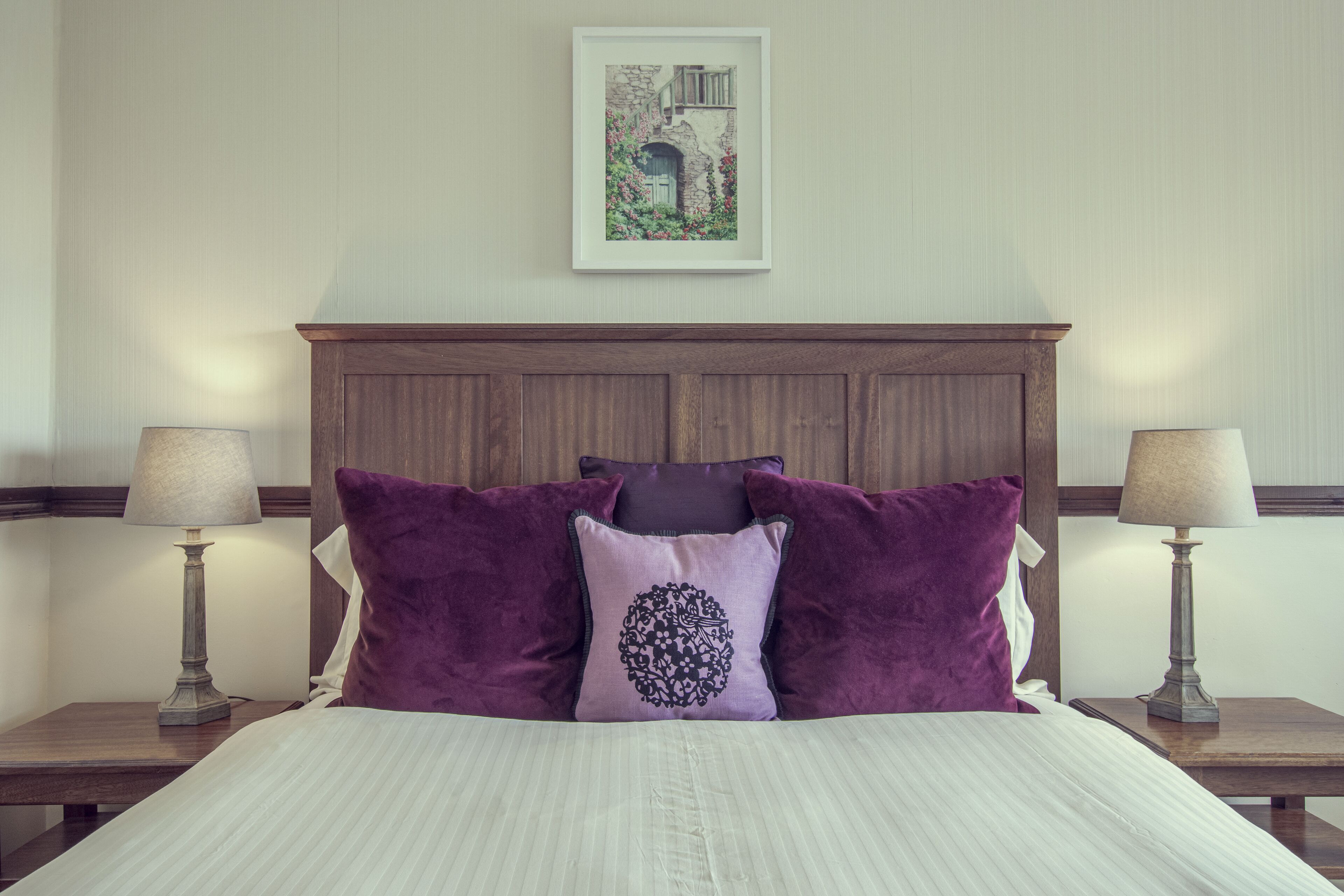 A neatly made bed with a headboard, two bedside tables with lamps, and a framed picture on the wall.