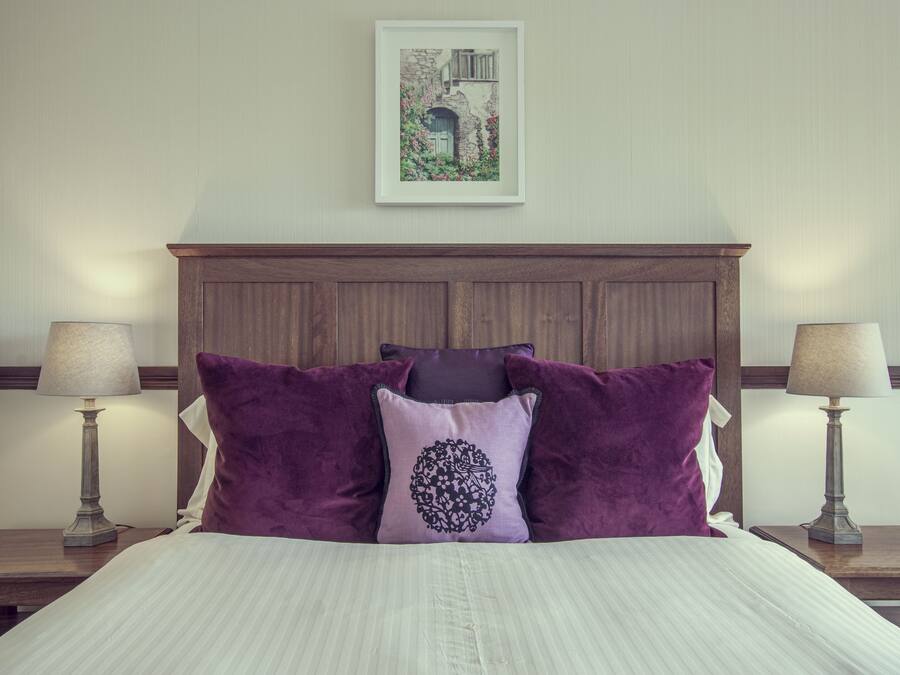 A neatly made bed with a headboard, two bedside tables with lamps, and a framed picture on the wall.