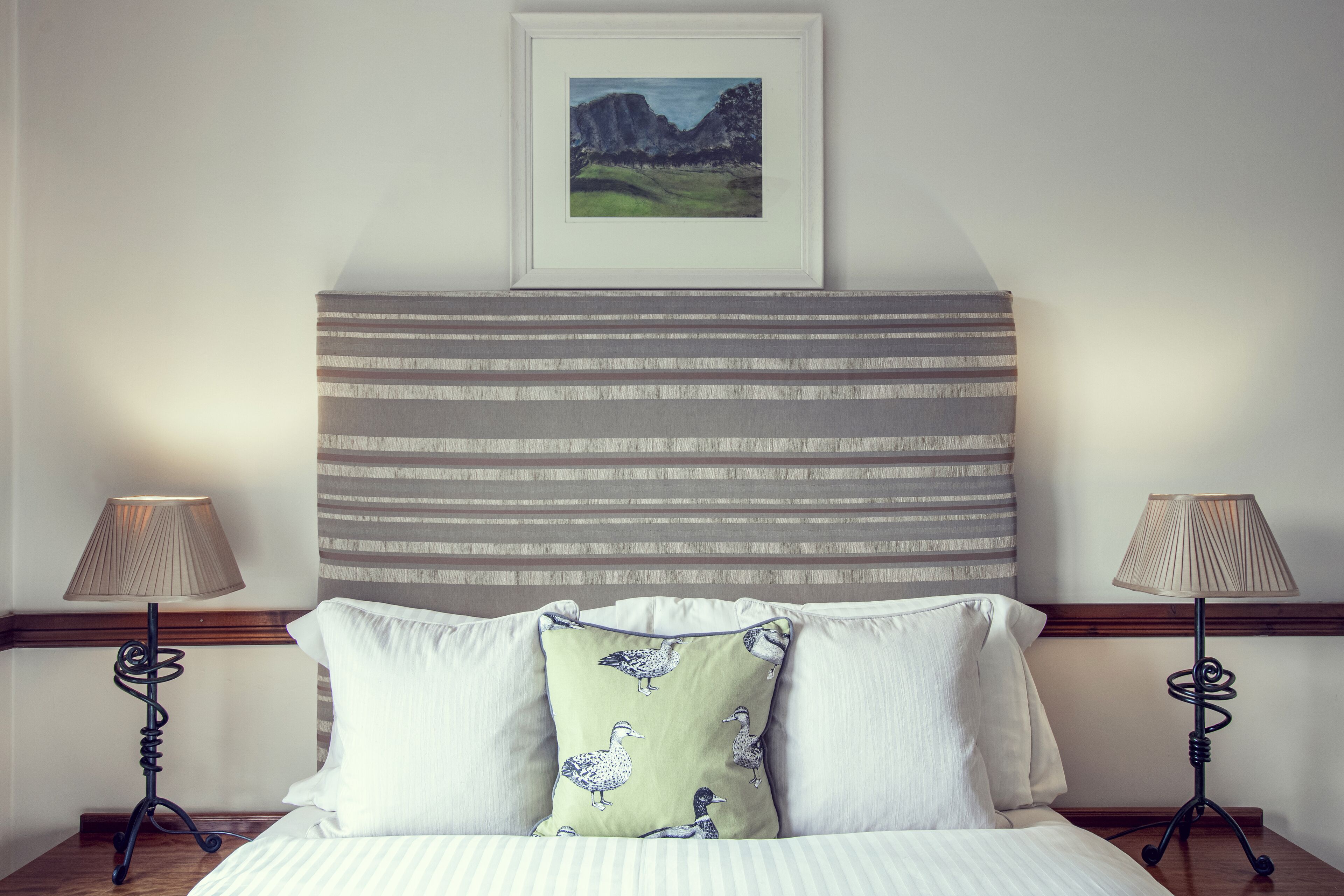 A neatly made bed with striped bedding, two bedside lamps, and a pillow with a bird pattern.