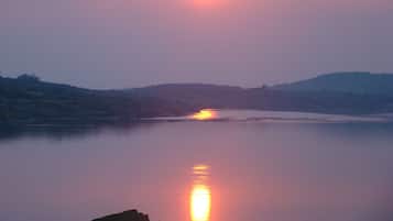 Un atardecer sobre un lago tranquilo con una costa lejana y colinas.