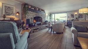 A cozy living room with a brick fireplace, comfortable seating, and a view of the outdoors. - The Ardagh Hotel & Restaurant (Clifden)