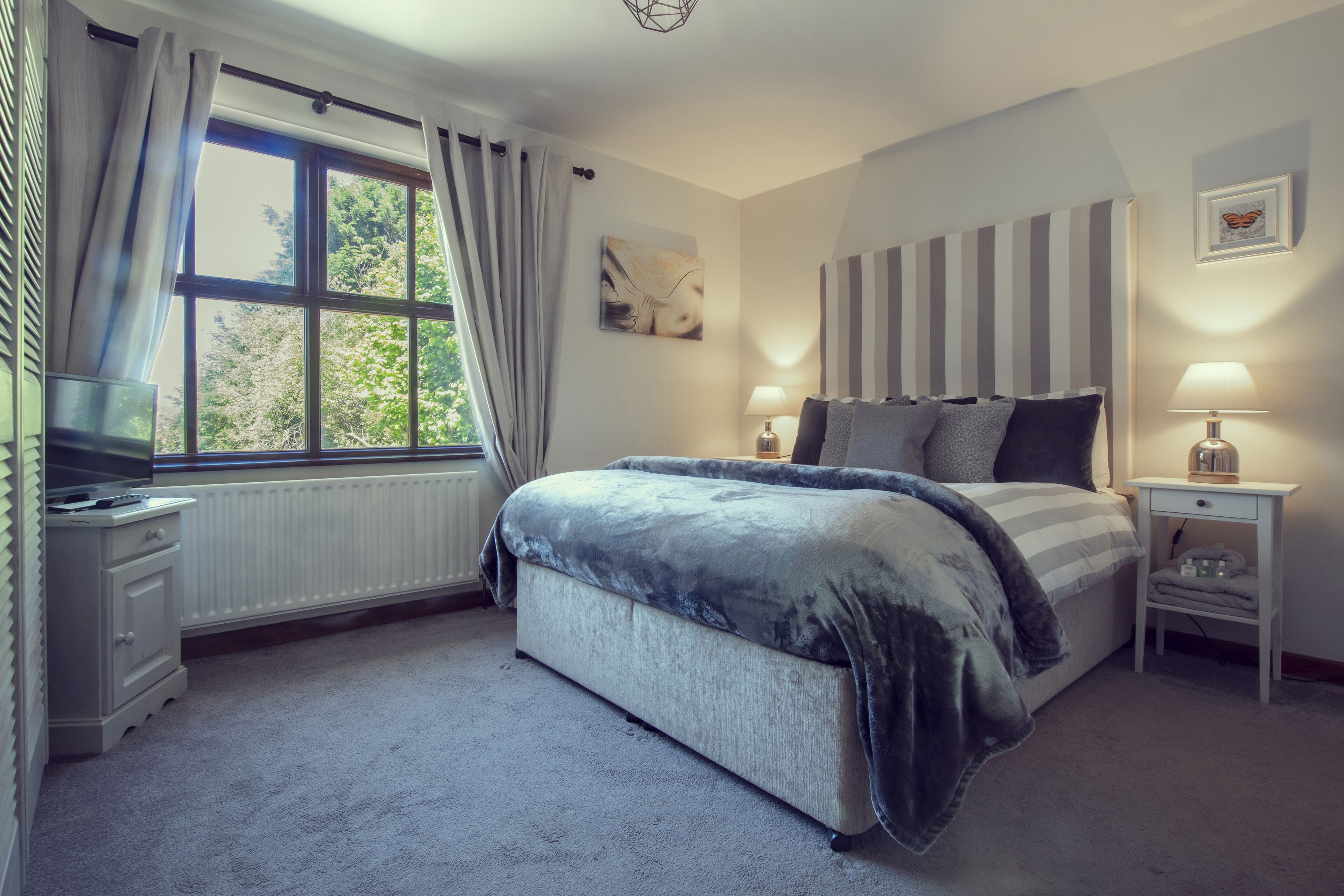 A bedroom with a large bed, bedside tables with lamps, a radiator, and a window with curtains.