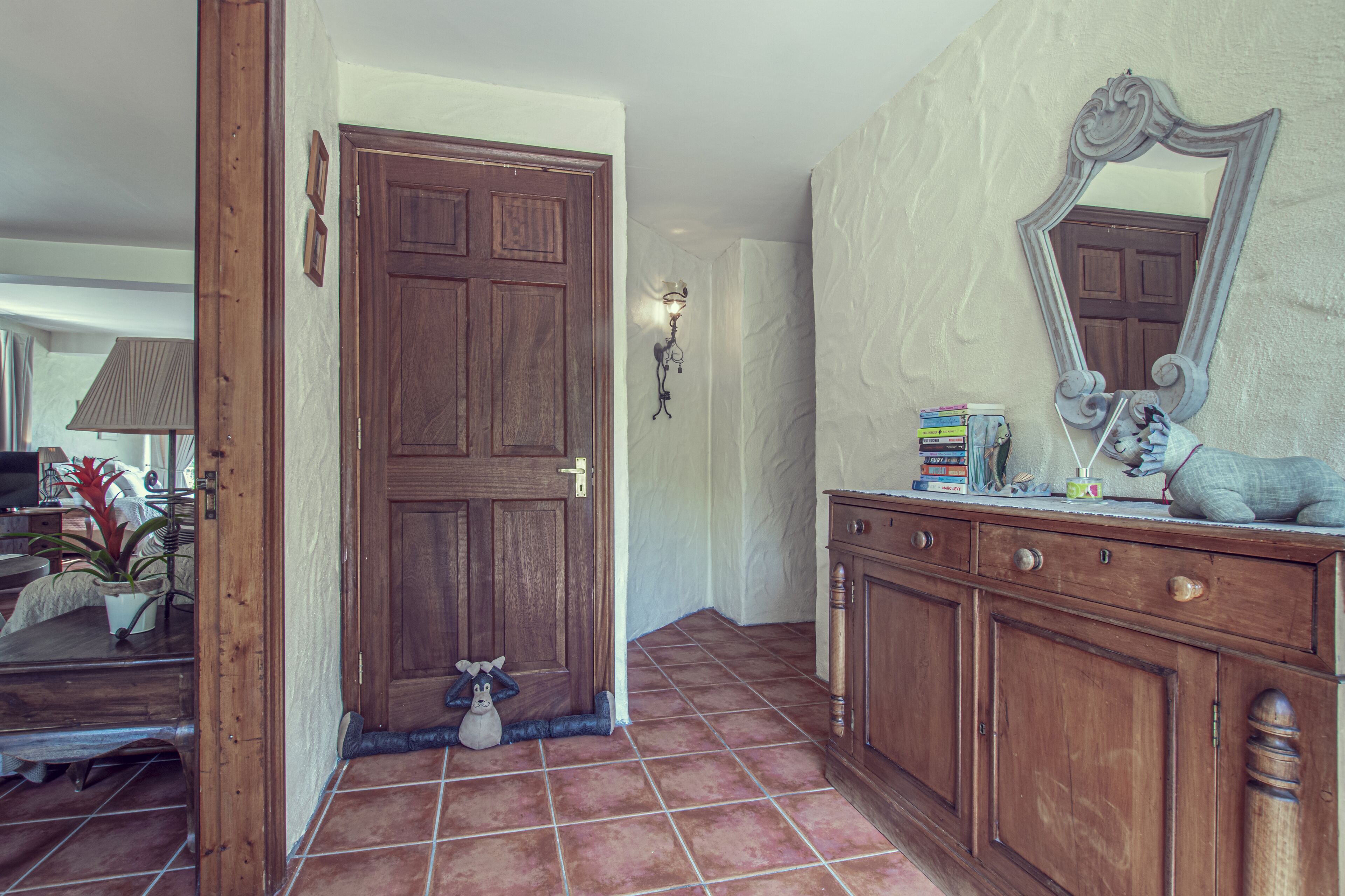 A hallway with a wooden door, a mirror, and a cabinet with books and decorative items.