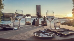 A table set for a meal with wine glasses, a bottle, and a candle, overlooking a body of water at sunset. - The Ardagh Hotel & Restaurant (Clifden)
