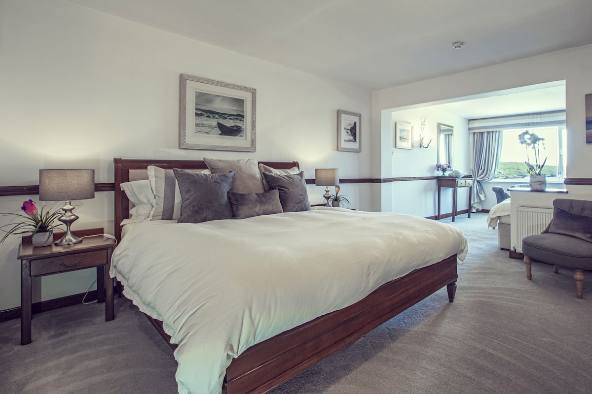 A bedroom with a large bed, bedside tables, a chair, a desk, and a view of the outdoors.