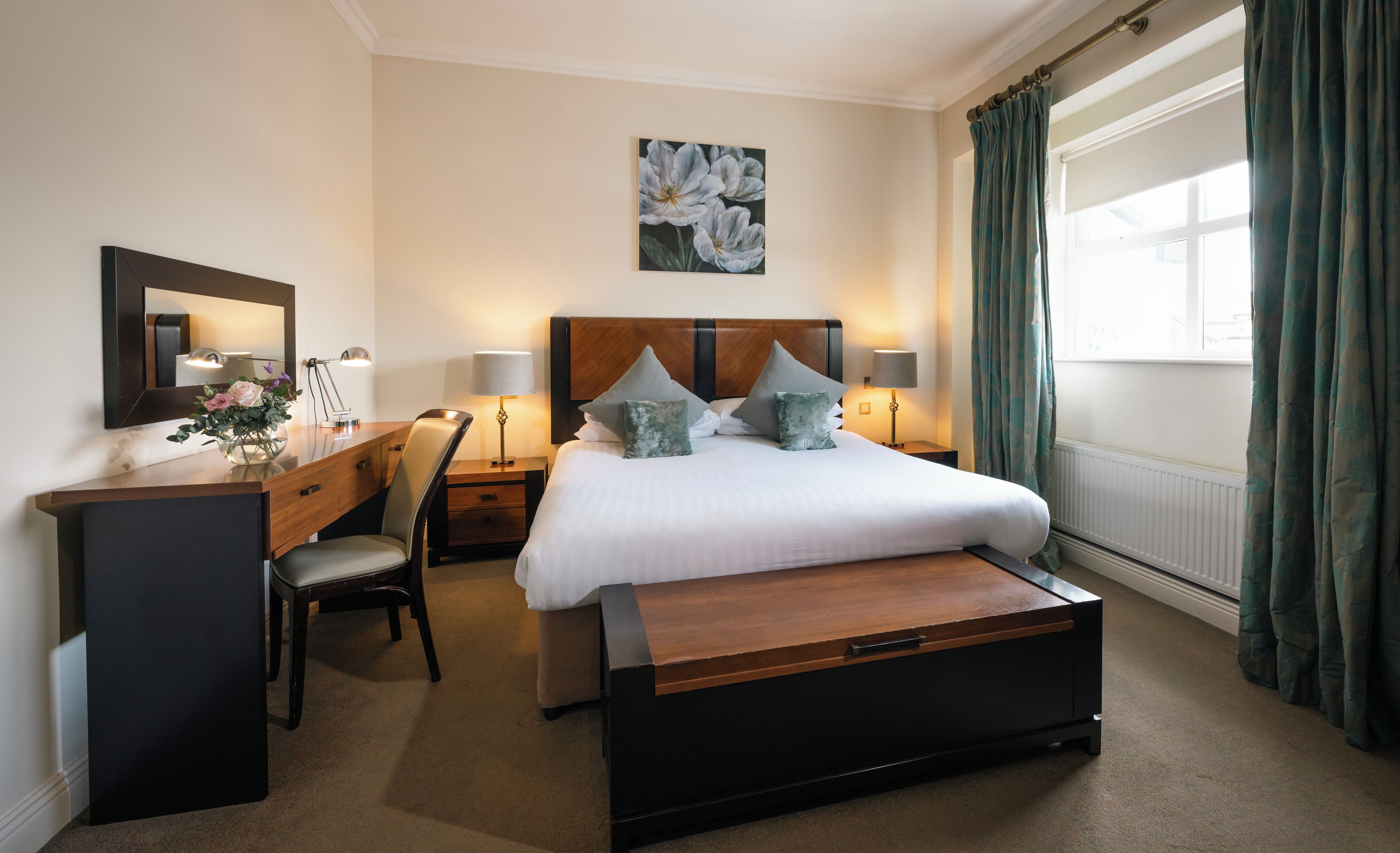 Habitación de hotel con cama, mesitas de noche, escritorio, silla, espejo y ventana con cortinas.