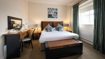 Habitación de hotel con cama, mesitas de noche, escritorio, silla, espejo y ventana con cortinas.
