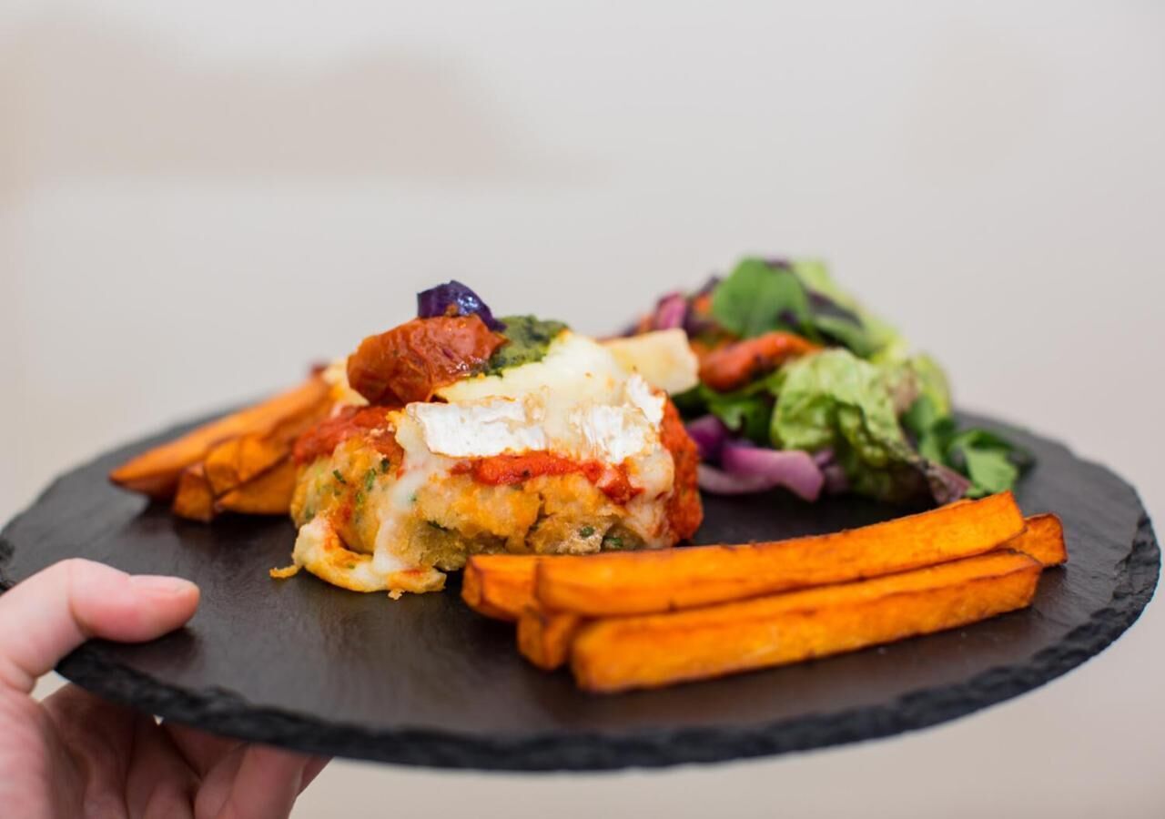 Una persona sosteniendo un plato de pizarra negra con una comida que incluye un plato al horno, zanahorias asadas y una ensalada.