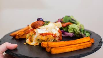 Una persona sosteniendo un plato de pizarra negra con una comida que incluye un plato al horno, zanahorias asadas y una ensalada.