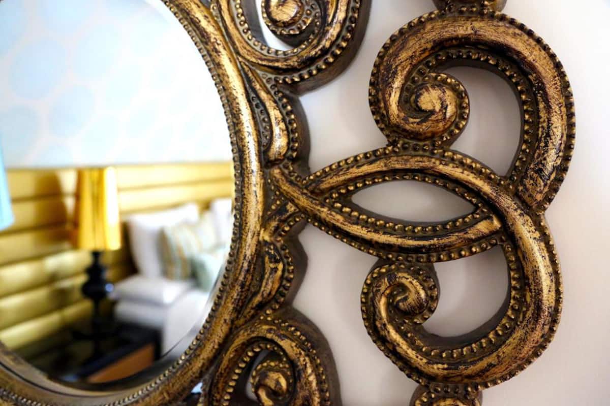 A close-up of an ornate, distressed gold-colored mirror frame with intricate designs.