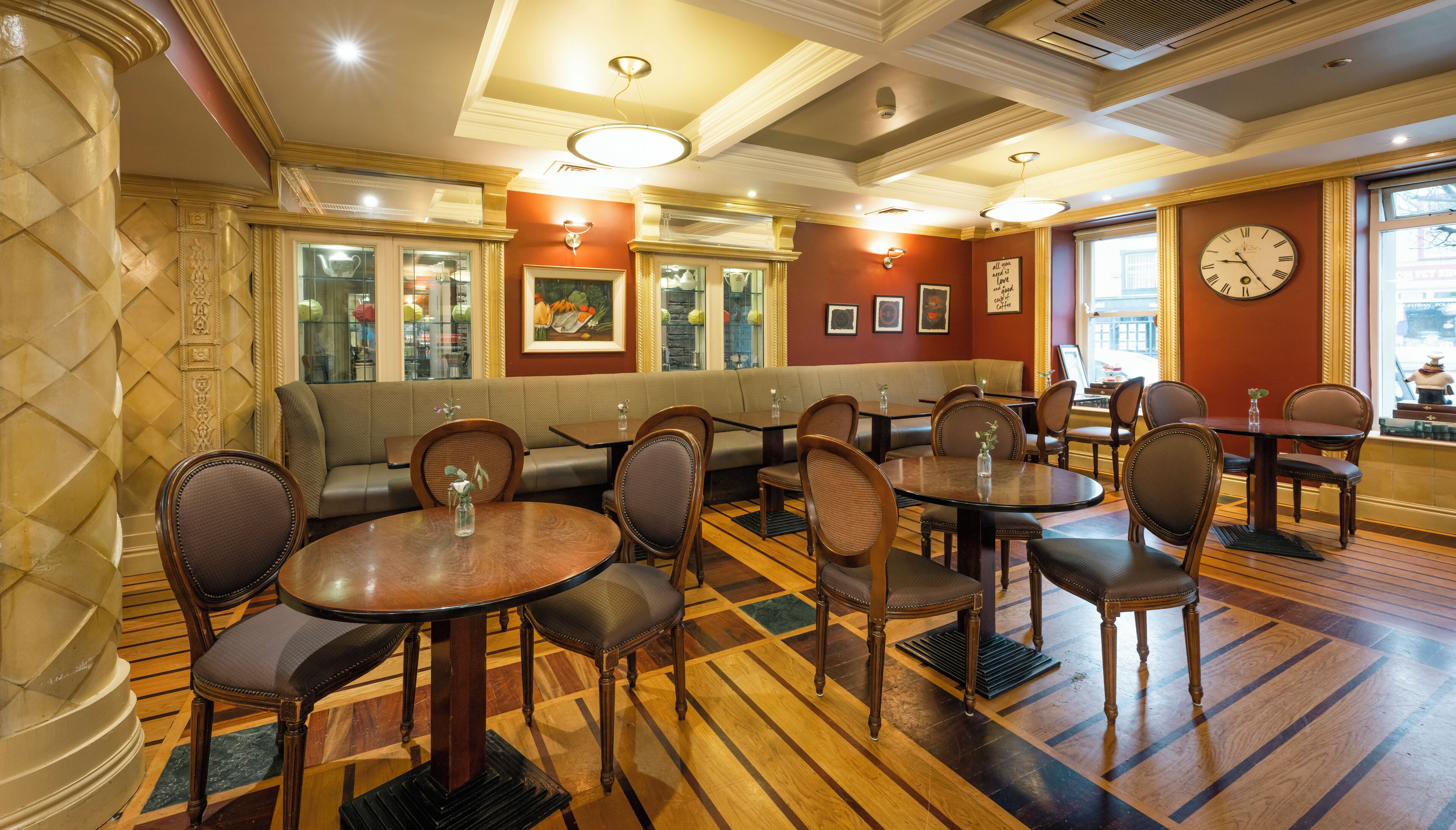 A restaurant with round tables and cushioned booths, wooden floors, and a clock on the wall.